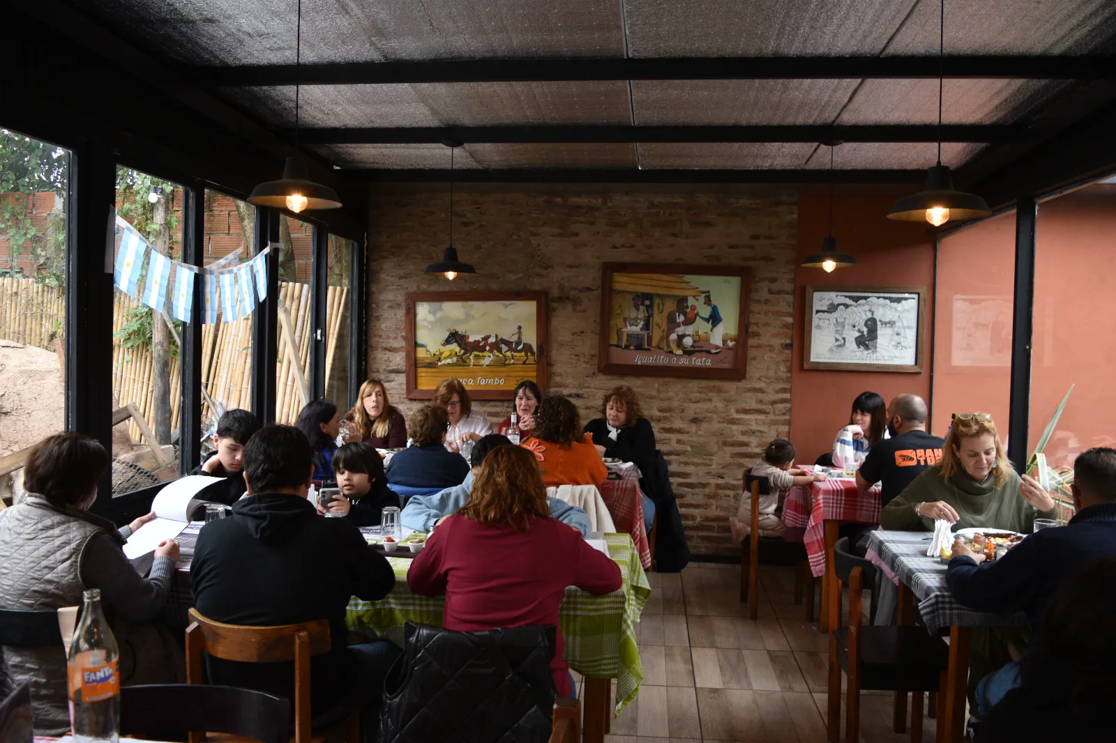 Salón del Bodegón Tras Cartón lleno de gente, con paredes de ladrillo y banderas argentinas