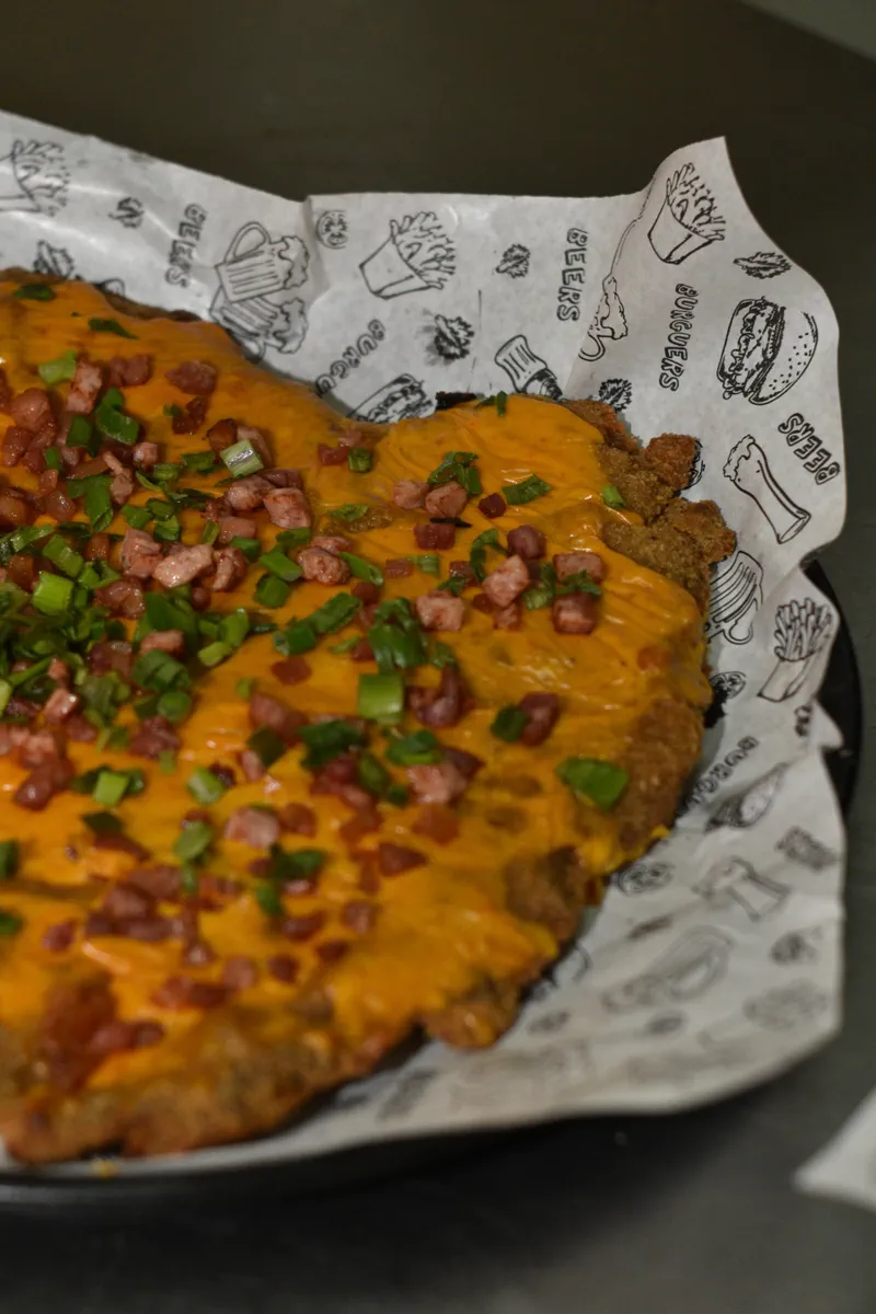 Milanesa cubierta de cheddar, panceta crocante y verdeo
